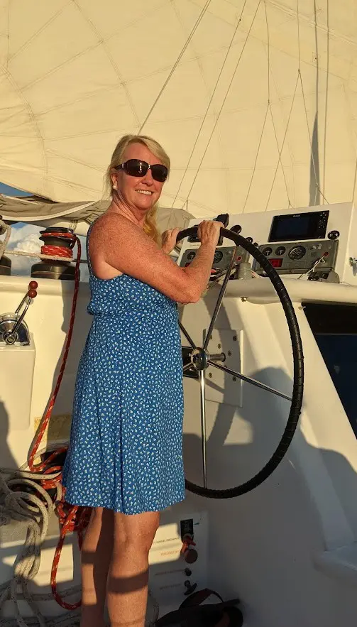 A woman holding onto the steering wheel of her boat.